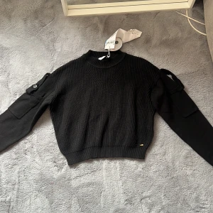 Svart kofta - Säljer en svart kofta med coola detaljer på armarna. Den är aldrig använd. Säljer för den är för liten, tröjan är storlek M men är liten i storleken! 