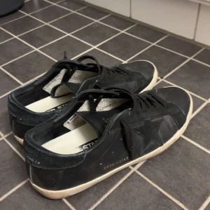 Svarta sneakers från Golden Goose - Säljer ett par svarta sneakers från Golden Goose med vit sula och klassisk stjärndetalj på sidan. Skorna har snörning och en låg profil, perfekt för en avslappnad och trendig stil.