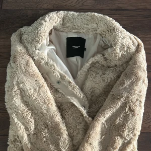 Beige teddyjacka från Vero Moda - Mysig och fluffig beige teddyjacka från Vero Moda. Jackan har lång ärm, knäppning framtill och är fodrad med ljus insida. Perfekt för kyligare dagar när du vill ha en trendig och bekväm look.