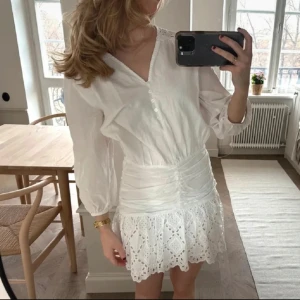 Studentklänning - Säljer en söt vit klänning med v-ringning och knappar framtill. Klänningen har trekvartsärmar och en fin spetskantad kjol. Perfekt för vår och sommar!