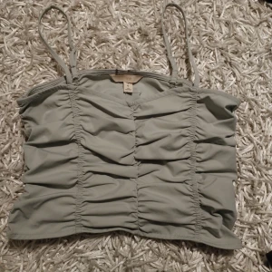 Ljusgrå croppad linnetopp från H&M - Säljer en ljusgrå croppad linnetopp från H&M med smala axelband och rynkade detaljer framtill och baktill. Perfekt för varma dagar och enkel att matcha med olika outfits. Hör av dig vid frågor ❤️