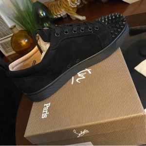Svarta sneakers med nitar från Christian Louboutin - Säljer ett par svarta sneakers från Christian Louboutin med mattsvarta nitar på tån och längs sidorna. Skorna har snörning och är tillverkade i mocka med svarta detaljer och rund tå. Perfekta för dig som vill sticka ut med en edgy stil.