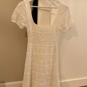 Vit virkad kortklänning från Zara - Superfin vit virkad klänning från Zara med korta puffärmar och rundad urringning. Klänningen har ett vackert geometriskt mönster och är perfekt för sommarens alla tillfällen. Sitter snyggt och har en feminin siluett.