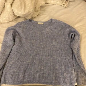 Ljusblå stickad tröja från ONLY - Säljer en mysig ljusblå stickad tröja från ONLY. Tröjan har en v-ringad hals och långa ärmar, perfekt för kyligare dagar. Den är i en mjuk och bekväm kvalitet som passar bra till både jeans och kjol.