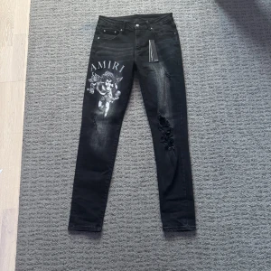 Amiri jeans - Snygga svarta jeans från Amiri med ett unikt ängeltryck på ena benet. Jeansen har en slim passform och slitna detaljer som ger en cool look. Perfekta för dig som vill sticka ut med stil.