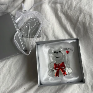 Kristallbjörn med hjärta - Söt kristallbjörn som håller ett hjärta med texten 'I LOVE YOU'. Björnen har en röd rosett och kommer i en elegant presentförpackning med silverdetaljer och en 'For you'-tag. Perfekt som en kärleksfull gåva.