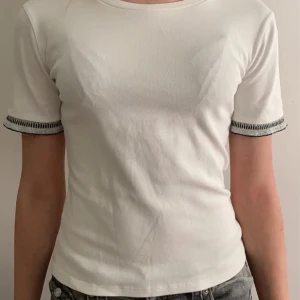 Trendig top - Säljer en stilren vit t-shirt med korta ärmar och kontrastsömmar vid ärmsluten. Perfekt för en avslappnad look. Passar bra till jeans eller shorts.