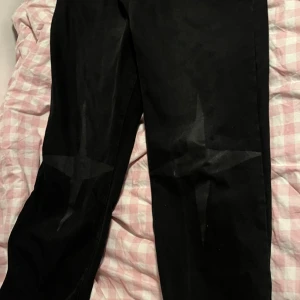 Svarta jeans med stjärndetaljer Baggy - Snygga svarta jeans med coola stjärndetaljer på benen och textdetaljer på bakfickorna. Perfekta för en trendig look. De har en klassisk passform och är tillverkade i ett slitstarkt material.