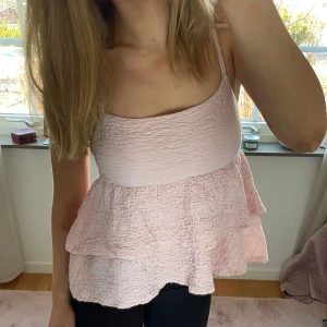 Rosa volanglinne - Säljer ett sött rosa linnetopp med volanger. Toppen har smala axelband och en luftig passform, perfekt för varma dagar. Den är tillverkad i ett lätt och bekvämt material.