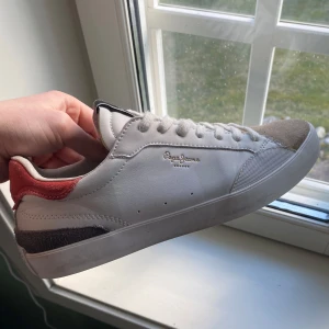 Vita sneakers från Pepe Jeans - Snygga vita sneakers från Pepe Jeans med mockadetaljer. Skorna är stilrena och har en klassisk design med märkets logga på sidan och tungan. Har en missfärgning som syns på bild 3, har blivit lite röd. Original lådan skickas med. Vid frågor eller funderingar är det bara att skicka ett dm💫