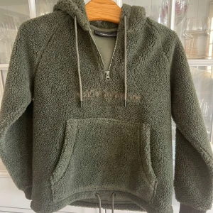 Grön fleece hoodie från Peak Performance ca 12 år - Mysig grön fleece hoodie från Peak Performance med dragkedja och justerbar dragsko i nederkant. Perfekt för kyliga dagar med sin varma och bekväma design. Stort känguruficka framtill för extra stil och funktion.