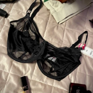 Svart mesh-bh - Snygg svart bh i transparent mesh med justerbara axelband och hakknäppning bak. Den har en stilren design med dekorativa ringdetaljer framtill. Perfekt för en elegant och modern look. Helt ny! Storlek UK 38J