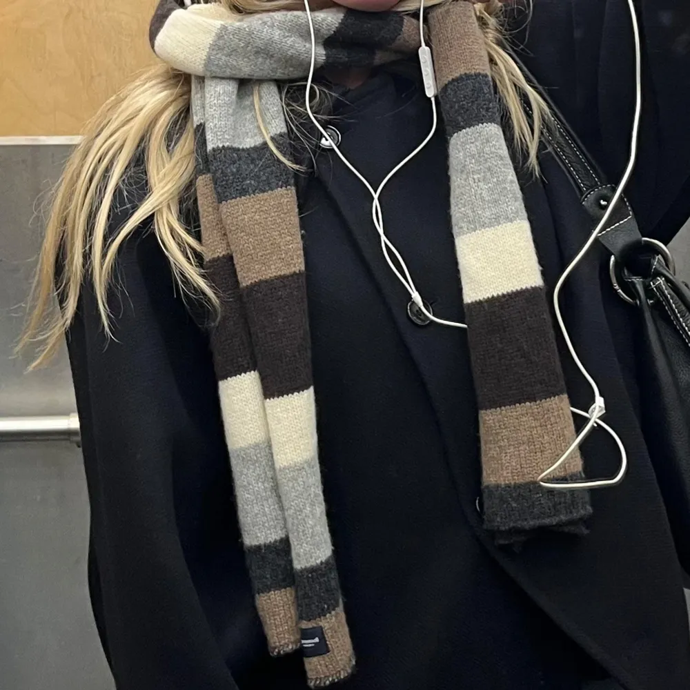 Snygg och mysig halsduk med breda ränder i jordnära färger som beige, brun och grå. Perfekt för att hålla sig varm under kyliga dagar. Den är i ull från boomerang🥰. Muu.