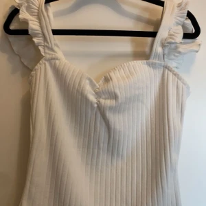 Vit ribbad topp med volangärmar - Säljer en söt vit ribbad topp med volangärmar. Toppen har en v-ringad design och är perfekt för sommarens varma dagar. Den är både stilren och bekväm, och passar till många olika outfits. Den är i ny skick från SHEIN i storlek XS