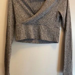Grå ribbad omlottopp - Snygg grå ribbad omlottopp med långa ärmar och croppad passform. Perfekt för en stilren look. Den är i nyskick från Shein i storlek S