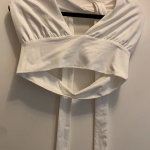 Vit ärmlös knytblus - Säljer en stilren vit ärmlös blus med knytband i midjan. Perfekt för en chic och elegant look. Blusen har en unik design med öppen rygg och breda axelband. Den är i ny skick från Shein i storlek S