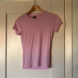 Rosa t-shirt från Gina Tricot - Säljer en söt rosa t-shirt från Gina Tricot. Den har en klassisk rund hals och korta ärmar, perfekt för en avslappnad stil. T-shirten är gjord i ett mjukt material som känns skönt mot huden. Perfekt för sommardagar eller som ett basplagg i garderoben.