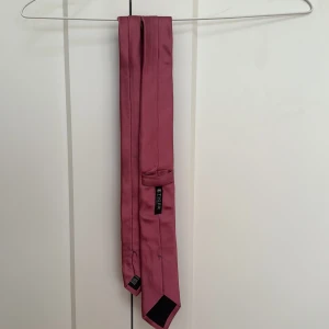 Rosa slips från Tiger of Sweden - Elegant rosa slips från Tiger of Sweden. Slipsen har en slät yta och en klassisk design som passar perfekt till balen eller skolavslutningen 