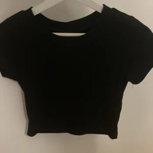 Svart croppad topp - Snygg svart croppad topp med korta ärmar. Perfekt för en stilren look. Passar bra till både jeans och kjol.