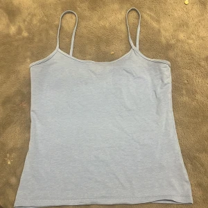 Ljusblå linne - Säljer en enkel och stilren ljusblå linnetopp med tunna axelband. Perfekt för varma sommardagar eller som ett basplagg i garderoben.