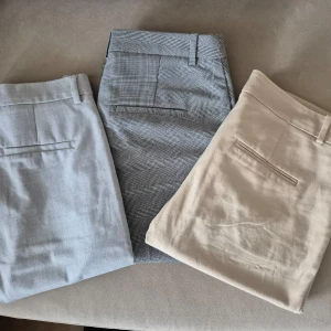 Tre par kostymbyxor i olika färger - Säljer tre par stilrena kostymbyxor. Ett par i ljusgrått, ett par i beige och ett par med rutigt mönster. Perfekta för en elegant look. Byxorna har en rak passform och är tillverkade i ett lätt och bekvämt material. Zara, hm och bershka, storlek 36