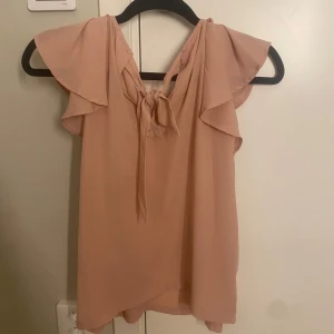 Beige/rosa blus från ONLY - Säljer en söt beige/rosa blus från ONLY med volangdetaljer och knytning bak. Nyskick och nästan aldrig använd. 