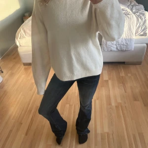 Vit stickad tröja - Säljer en mysig vit stickad tröja med rund hals och långa ärmar. Perfekt för kyliga dagar och enkel att matcha med olika outfits. Tröjan har en klassisk design med ribbade muddar vid ärmslut och nederkant.