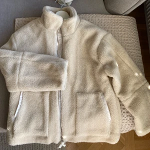 Vit teddyjacka med dragkedja - Helt oanvänd mysig vit teddyjacka med dragkedja och hög krage. Jackan har långa ärmar och två praktiska fickor framtill. Säljer jacka då den är för liten för mig. 