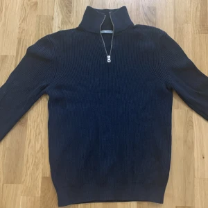 Mörkblå stickad tröja från Zara - Säljer en stilren mörkblå stickad tröja från Zara med dragkedja vid halsen. Perfekt för kyligare dagar med sin höga krage och långa ärmar. Tröjan har en ribbad struktur som ger en snygg passform. Ny pris 700 kr 