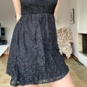 Svart spetsklänning - Snygg svart spetsklänning med korta ärmar och hög hals. Klänningen har ett vackert blommigt mönster och en elegant passform som passar perfekt för festliga tillfällen.