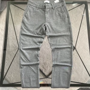 Grå byxor från Only & Sons - Snygga grå byxor från Only & Sons i en klassisk stil. De har en normal passform med midwaist och är tillverkade i ett mjukt bomullsmaterial. Byxorna har både knappar och dragkedja samt praktiska fickor fram och bak.