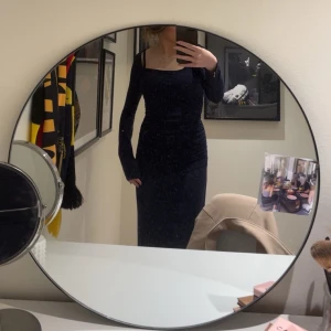 Mörkblå klänning med rynkdetaljer - Snygg mörkblå långklänning med långa ärmar och rynkdetaljer längs sidan. Klänningen har en tight passform och är tillverkad i ett mjukt material.