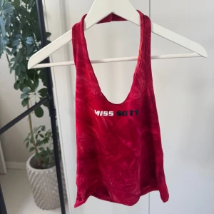 Röd linnetopp från Miss Sixty - Snygg röd linnetopp från Miss Sixty med ett coolt tryck på framsidan. Perfekt för en trendig look. Toppen har en djup urringning och ärmlös design.