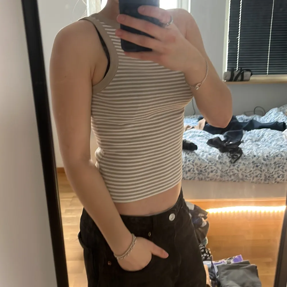 Säljer en randig linnetopp i beige och vit. Toppen är ärmlös och croppad, perfekt för varma dagar. Den har en tight passform och är superbekväm att bära.. Yläosat.