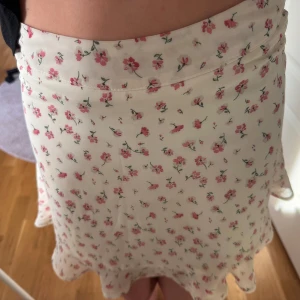 Blommig kjol  - Söt blommig kjol från Shein i vitt med rosa blommor. Kjolen har en volangdetalj längst ner och en kort längd som passar perfekt för varmare dagar.