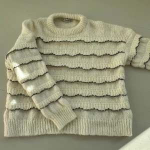 Vit stickad tröja från Zara - Säljer en mysig vit stickad tröja från Zara med svarta vågiga ränder. Tröjan har en rund halsringning och långa ärmar. Perfekt för kyliga dagar!