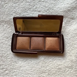 Hourglass Ambient Lighting Palette Volume III - Snygg bronzerpalett från Hourglass med tre olika nyanser i en elegant brun förpackning. Perfekt för att skapa en solkysst look. Inkluderar en praktisk spegel i locket. Endast testad.