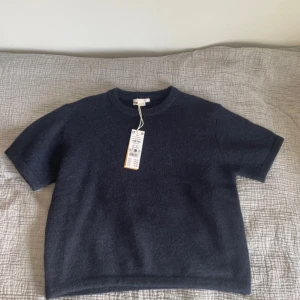 Mörkblå stickad kortärmad topp - En stilren mörkblå stickad topp med korta ärmar och rund hals. Toppen har en mjuk och lite fluffig känsla, perfekt för lager-på-lager eller att bära som den är. Enkel och clean design som funkar till många olika looks.