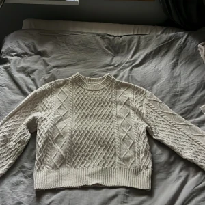 Beige stickad tröja med flätmönster - Säljer en beige stickad tröja med snyggt flätmönster och ribbade muddar. Tröjan har rund halsringning och långa ärmar. Perfekt för dig som gillar en klassisk men trendig look till höst och vinter.