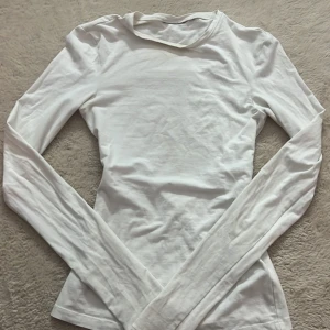Vit långärmad tight topp - Säljer en vit långärmad topp i tight passform. Tröjan är enkel och stilren med rund halsringning och stretchigt material som sitter snyggt mot kroppen. Perfekt att styla med jeans eller kjol för en clean look.Köpt på weekday för ca 200kr❣️