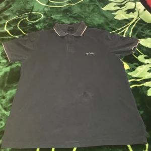 Mörkblå pikétröja från Hugo Boss - Snygg mörkblå pikétröja från Hugo Boss med klassisk krage och två knappar framtill. Tröjan har diskret logga på bröstet och kontrastdetaljer på kragen. Perfekt för en clean och stilren look. Tillverkad i bomull för skön känsla.