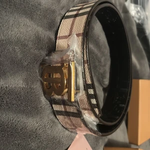  rutig skärp med guldspänne guldig B logga - Säljer nu mitt bälte för att den inte passade mig säljer den vidare så slipper den samla damm helt nytt bälte plasten är kvar på B loggan om de är nå frågor är det bara att fråga på. Pris kan alltid diskuteras först till kvarn🙂