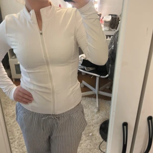 Vit träningsjacka från Relode S - Slimmad och sportig vit träningsjacka från Relode i storlek S. Jackan har hel dragkedja framtill, hög krage och långa ärmar. Perfekt för gymmet eller powerwalks. Snygg och clean design med diskret logga på bröstet.