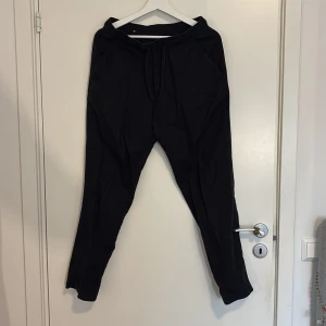 Svarta mjukisbyxor från Zara - Svarta linnebyxor från Zara med elastisk midja och snörning. Byxorna har en avslappnad passform, sidfickor och är tillverkade i ett mjukt material som känns skönt mot huden. Perfekta för chill dagar eller när du vill vara bekväm men ändå se stilren ut.