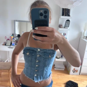 Ljusblå jeans tubtopp med knappar - Säljer en ljusblå jeans tubtopp med snygga silverfärgade knappar framtill och rå, fransig nederkant. Toppen har två fejkade bröstfickor och smockad baksida för skön passform. Perfekt till sommarens alla outfits!