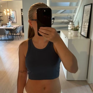 Mörkblå ribbad croppad linnetopp - Säljer en mörkblå croppad linnetopp med ribbad struktur. Toppen är ärmlös med breda axelband och rund halsringning, perfekt för en chill och stilren look. Enkel att matcha med både jeans och kjol. Aldrig använd utan prislapp