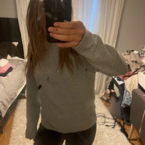 Grå stickad tröja med lång ärm - Mysig grå stickad tröja med lång ärm och klassisk rund hals. Perfekt för kyliga dagar och enkel att matcha med jeans eller leggings. Tröjan har en normal passform och är superbekväm att bära.