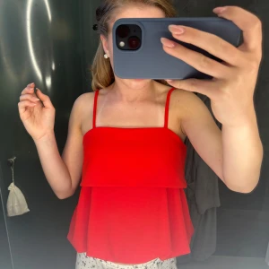 Röd voluminös linnetopp med smala band - Säljer en röd linnetopp med smala axelband och voluminös, lös passform. Toppen har en snygg volangdetalj upptill som ger extra dimension och en luftig känsla. Perfekt för dig som vill sticka ut med en färgstark och trendig look.