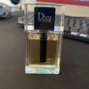 Dior Homme parfym 50ml - Dior Homme parfym i en stilren, rektangulär glasflaska med svart lock och tydlig logga. Doften är maskulin och elegant, perfekt för dig som gillar exklusiva parfymer. Flaskan rymmer 100ml och har en transparent design med ljusgul vätska.