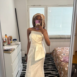 Balklänning - Säljer en elegant vit långklänning med axelbandslös design och stor rosettdetalj framtill. Har bara haft på mig den 1 gång